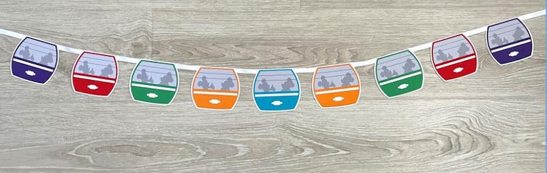 May include: A colourful garland featuring a string of paper cutouts of a classic amusement park ride. The cutouts are in shades of blue, red, green, orange, and teal, and each features a silhouette of people riding in a gondola.