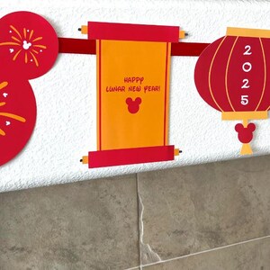 Puede incluir: Bandera roja y dorada del A&ntilde;o Nuevo Chino con orejas de Mickey Mouse, un rollo con el texto "&iexcl;Feliz A&ntilde;o Nuevo Lunar!", una linterna roja con "2025" en ella y un sobre rojo con una cabeza de Mickey Mouse.