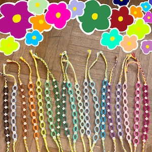 Könnte beinhalten: Eine Sammlung von 18 bunten Freundschaftsarmbändern mit einem Gänseblümchenmuster. Die Armbänder sind aus buntem Stickgarn gefertigt und in einem Regenbogenmuster angeordnet.