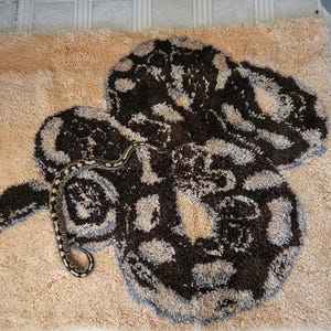 May include: A brown and white snake patterned rug with a real snake curled on top of it.