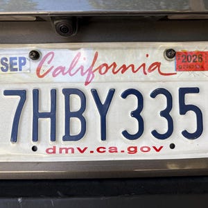 May include: A California license plate with the text "California" in red script. The plate number is 7HBY335 in dark blue. The plate has a sticker for 2026 and the website address "dmv.ca.gov".