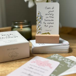 May include: A set of "Words of Blessings" cards with a wooden card holder. The cards have floral designs and inspirational quotes. The text on the displayed card reads "Cast all your anxiety on him because he cares for you."
