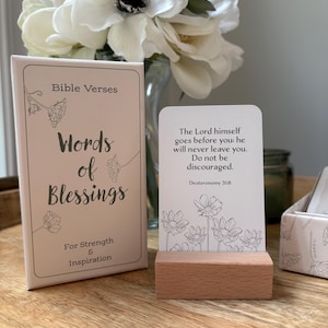 May include: A set of "Words of Blessings" Bible verse cards with a wooden card holder. The box and cards are light pink with floral illustrations and text. The displayed card reads "The Lord himself goes before you: he will never leave you. Do not be discouraged."