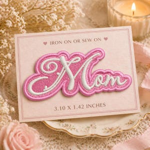 May include: A pink embroidered patch with the word "Mom" in a cursive script, outlined in white. The patch is on a pink card that reads "Iron on or Sew on." The patch measures 3.10 x 1.42 inches.