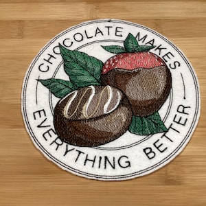May include: Embroidered patch with chocolate-covered strawberries and a truffle, with green leaves. The circular patch has the words "CHOCOLATE MAKES EVERYTHING BETTER" in white lettering.