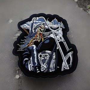 May include: Embroidered patch featuring a skeleton rider on a black motorcycle. The rider is wearing a blue hooded cloak and holding a flag. The patch has a black border and is set against a gray background.