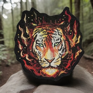 May include: Embroidered patch featuring a tiger's face with fiery orange, red, and yellow details. The tiger has green eyes and white stripes on its face. The patch is outlined in black and has a forest background.