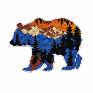 May include: Embroidered bear-shaped patch with a mountain and forest scene. The bear is outlined in white, with a blue body and a landscape of orange, brown, and blue. Suitable for attaching to clothing or accessories, this patch is a decorative item.