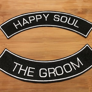 Peut inclure: Deux écussons brodés noirs incurvés avec des bordures blanches. L'écusson du haut présente le texte blanc HAPPY SOUL, et l'écusson du bas présente le texte blanc THE GROOM. Les deux écussons ont un design arqué épuré avec des lettres majuscules.