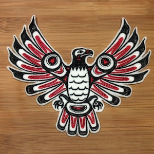 Op de afbeelding: Geborduurde patch met een gestileerde adelaar met uitgespreide vleugels. Het ontwerp gebruikt zwart, rood en wit, met gedetailleerde patronen. De patch is geschikt voor kleding of accessoires.