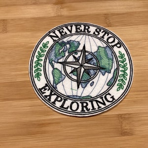 May include: Round patch with the words "NEVER STOP EXPLORING" encircling a compass rose and a world map. The map is green and blue, and the compass is gray. The patch has a white background and a black border.