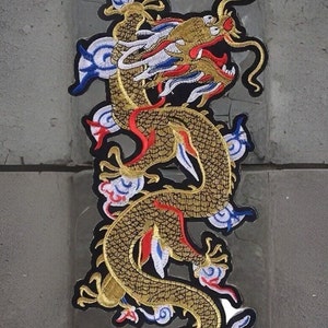 May include: Embroidered patch of a golden dragon with red, white, and blue details. The dragon is in a winding pose against a black backdrop, with cloud-like designs.
