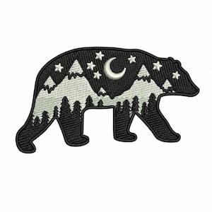 May include: Embroidered bear-shaped patch with a night scene design. The black bear has white mountains, trees, stars, and a crescent moon. Ideal for customising jackets, bags, or other fabric items.