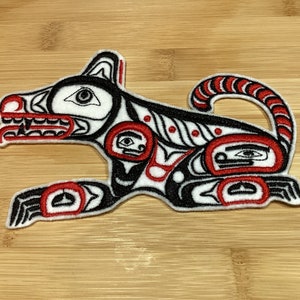 May include: Embroidered patch featuring a stylized dog design in black, white, and red. The patch has a running dog motif with intricate details, including eye and body shape designs. The patch is likely for clothing or accessories.