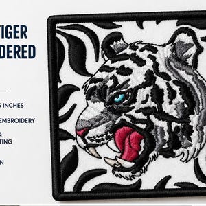 May include: Embroidered patch depicting a white tiger with blue eyes and an open mouth, set against a black and white background. The patch measures 8.5 x 8.3 cm and has a black border. Text on the patch reads "WHITE TIGER EMBROIDERED PATCH".