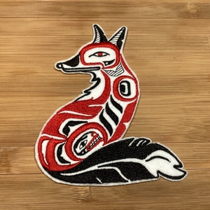 Può includere: Toppa ricamata con un disegno di volpe stilizzata in rosso, nero e bianco. La volpe è raffigurata in posizione seduta con motivi intricati, in uno stile artistico nativo americano. La toppa è probabilmente per abbigliamento o accessori.