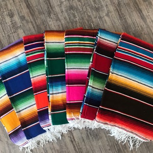 May include: A set of seven colorful Mexican blankets with fringe. The blankets are striped in various colors, including red, orange, yellow, green, blue, purple, and black.