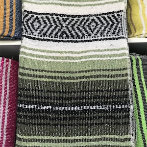May include: A folded green, white, and black woven blanket with a geometric diamond pattern. The blanket has horizontal stripes in varying shades of green and black. The edges have a white fringe.