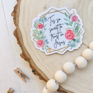 May include: A floral sticker with a gold geometric frame and the text "'Tis so sweet to trust in Jesus".