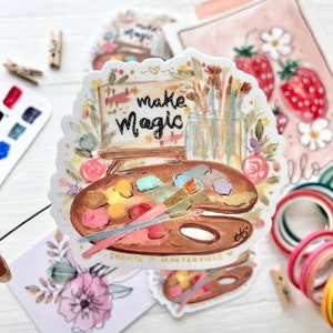 May include: A watercolor sticker featuring a paint palette, paintbrushes, a jar of brushes, and a small easel with the words "make magic" written on it. The sticker also includes the words "create a masterpiece" and a heart.