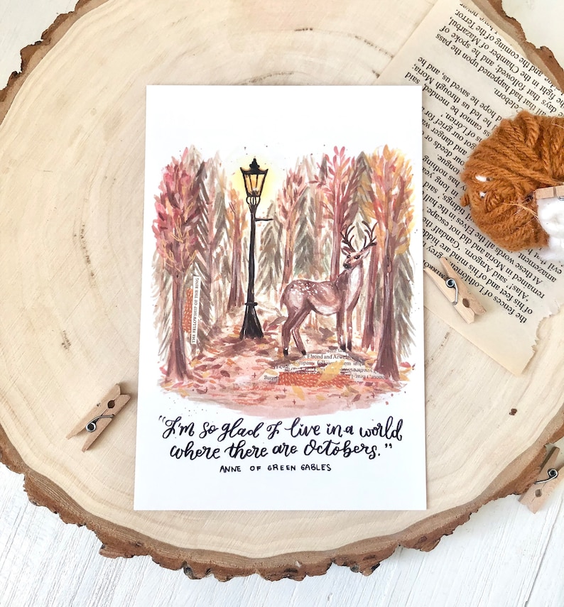 May include: A watercolor illustration of a deer standing in a forest with a streetlight in the background. The quote "I'm so glad I live in a world where there are Octobers." by Anne of Green Gables is written below the image.