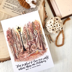 May include: A watercolor illustration of a deer standing in a forest with a street lamp and the quote "I'm so glad I live in a world where there are Octobers." from Anne of Green Gables.