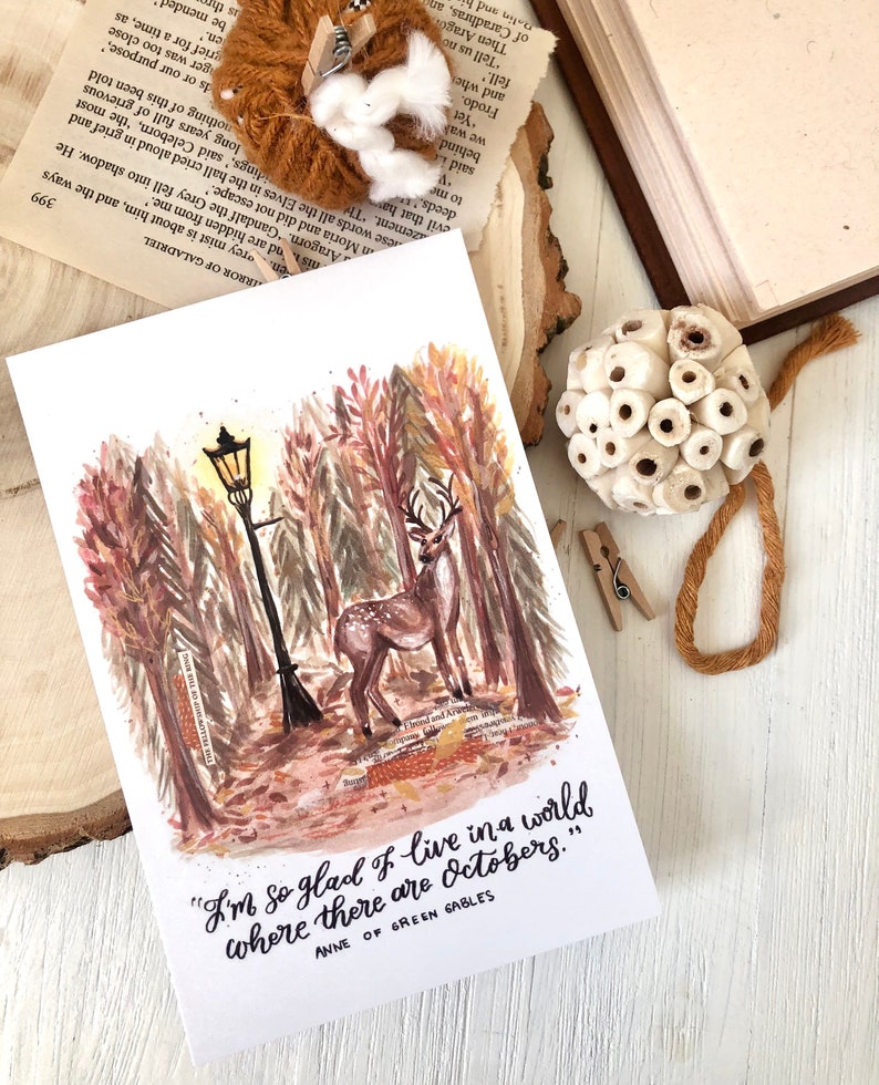 May include: A watercolor illustration of a deer standing in a forest with a street lamp and the quote "I'm so glad I live in a world where there are Octobers." from Anne of Green Gables.