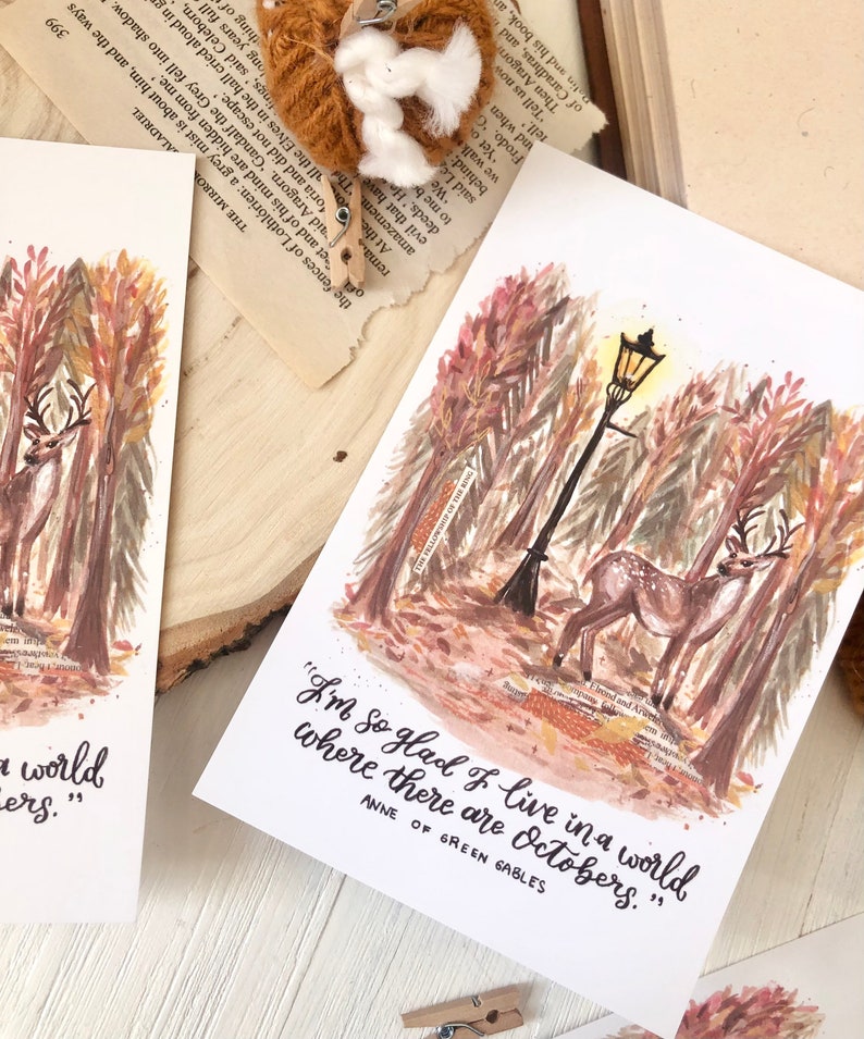 May include: A watercolor illustration of a deer walking through a forest with a street lamp in the background. The quote "I'm so glad I live in a world where there are Octobers." is written below the image, attributed to Anne of Green Gables.