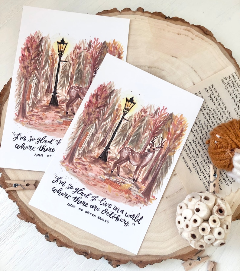 May include: A watercolor illustration of a forest scene with a deer and a streetlight. The quote "I'm so glad I live in a world where there are Octobers." is written below the image. The quote is attributed to Anne of Green Gables.
