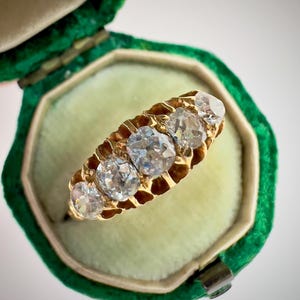 Puede incluir: Un anillo de oro con cinco diamantes redondos engastados en una banda texturizada. El anillo está en una caja de anillo de terciopelo verde.