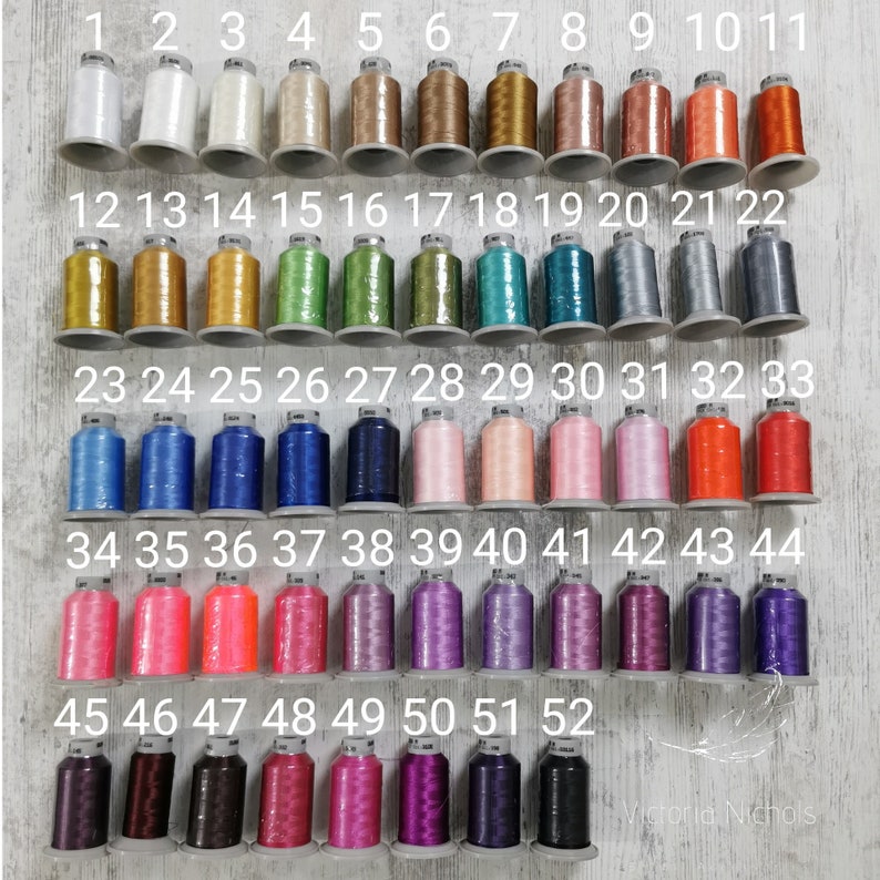 Puede incluir: Una colecci&oacute;n de 52 carretes de hilo para bordar, numerados del 1 al 52. Los carretes est&aacute;n dispuestos en filas de 11, con la &uacute;ltima fila que tiene solo 2 carretes. Los colores del hilo van del blanco al negro, con muchos tonos de rosa, azul, verde y naranja.