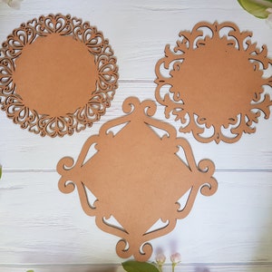May include: Three decorative wooden plaques with intricate cut-out designs. The plaques are brown and have a circular and square shape.