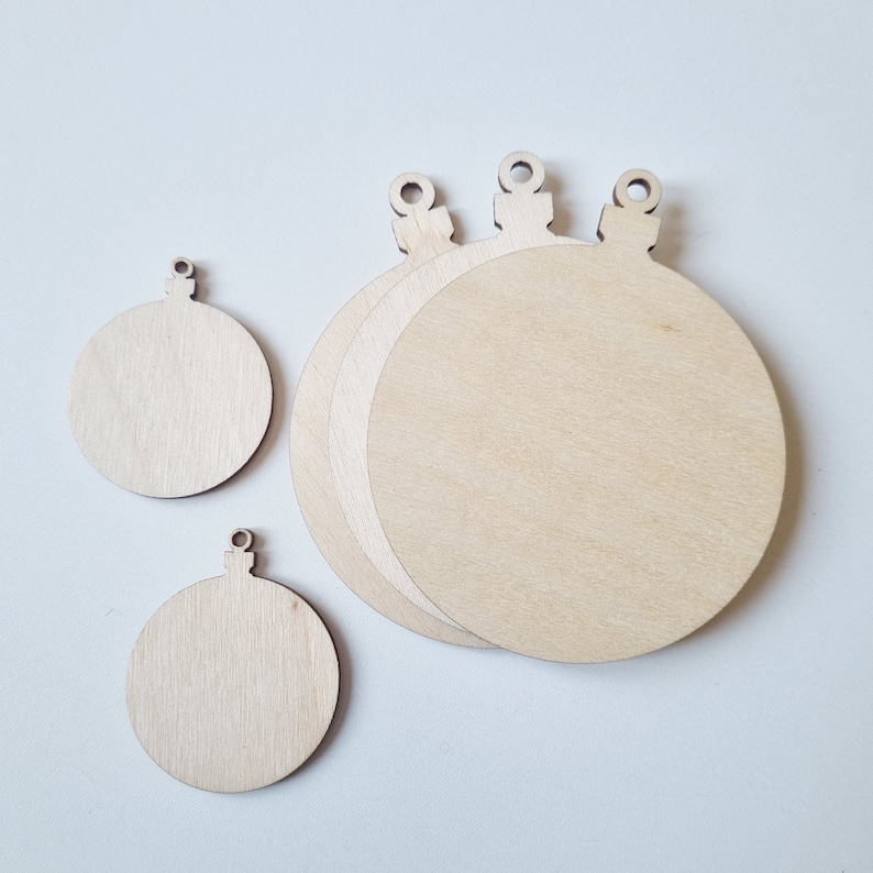 May include: Four unfinished wooden ornaments in the shape of Christmas tree baubles. The ornaments are various sizes and have a hole at the top for hanging.