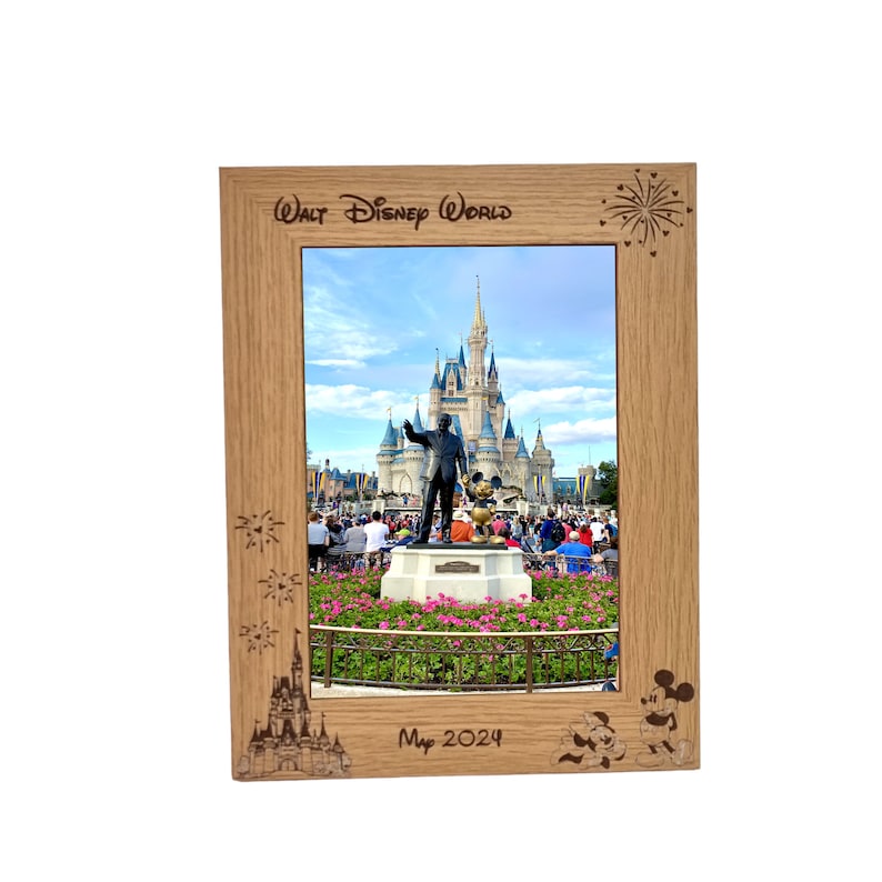 May include: A wooden picture frame featuring a photograph of Cinderella's Castle at Walt Disney World. The frame is engraved with "Walt Disney World", fireworks, Mickey Mouse, and the date "May 2024".