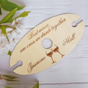 May include: Wooden wine bottle holder with two cutouts for glasses. The holder is engraved with the text "Best wines are ones we drink together" and the names "Jasmine" and "Niall".
