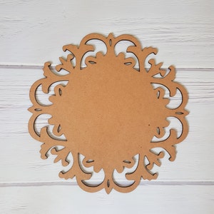 May include: A brown wooden round decorative plaque with a cutout design of intricate swirls and floral patterns.