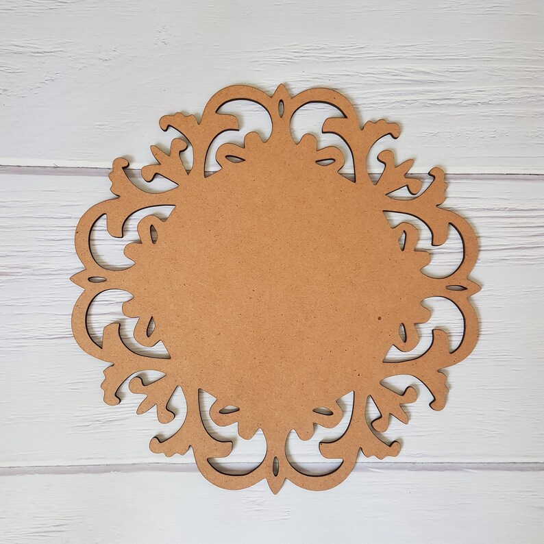 May include: A brown wooden round decorative plaque with a cutout design of intricate swirls and floral patterns.