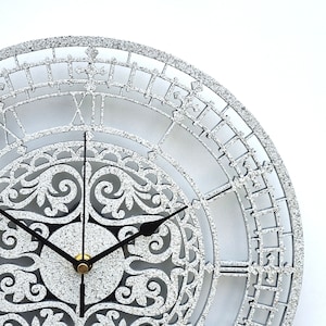 May include: A silver glitter clock with Roman numerals and a decorative, ornate design. The clock face has a silver glitter background with black hands.