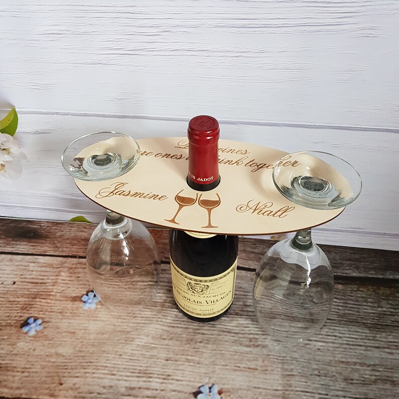 May include: Wooden wine bottle holder with two glass holders. The holder has the text "Good wines are ones we drink together" and the names "Jasmine" and "Niall".
