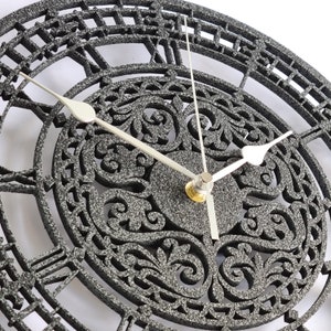 May include: A black and silver clock with Roman numeral markings and a detailed floral design. The clock has a silver hand and a silver center piece.