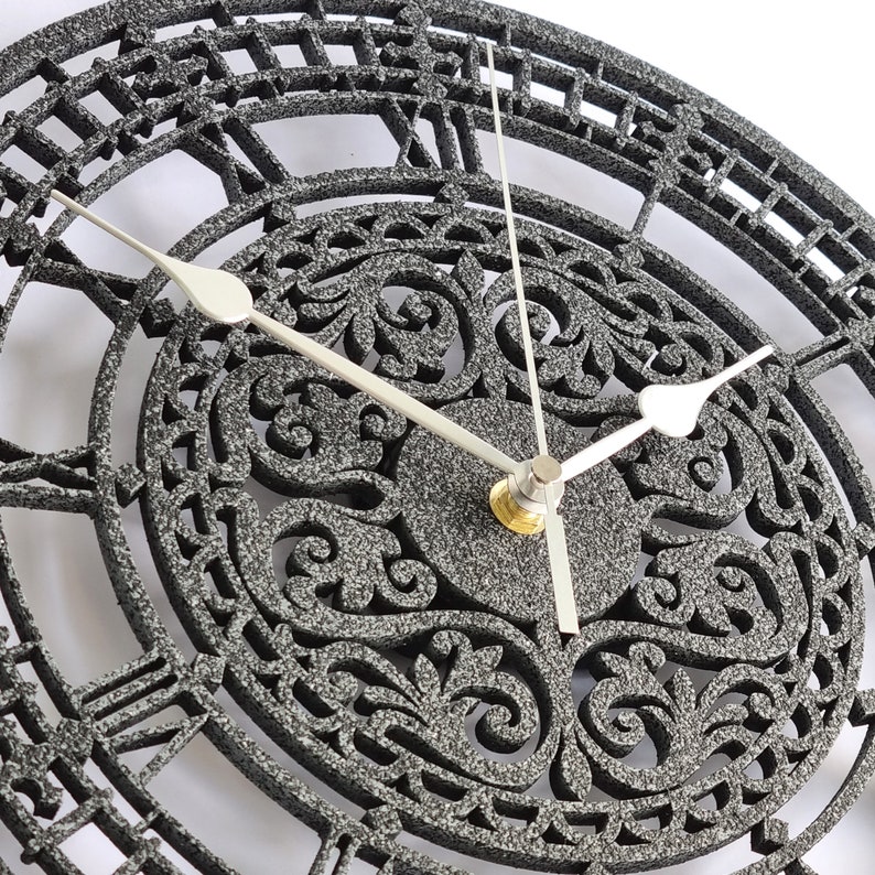 May include: A black and silver clock with Roman numeral markings and a detailed floral design. The clock has a silver hand and a silver center piece.