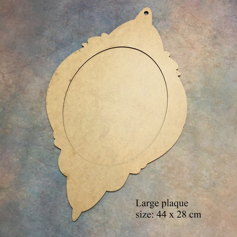 Pode incluir: Uma placa de madeira grande, n&atilde;o pintada, com um recorte oval no centro. A placa tem uma borda decorativa e adornada e um furo na parte superior para pendurar. Mede 44 x 28 cm.