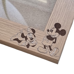 May include: A wooden picture frame with a light brown finish. The frame has a cutout of Mickey Mouse and Minnie Mouse on the bottom right corner.