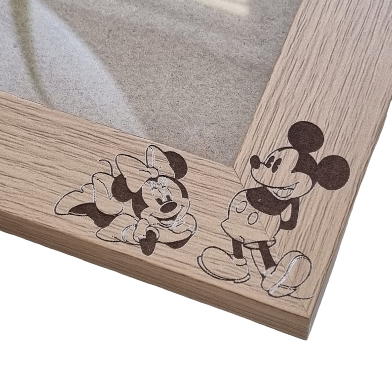 May include: A wooden picture frame with a light brown finish. The frame has a cutout of Mickey Mouse and Minnie Mouse on the bottom right corner.