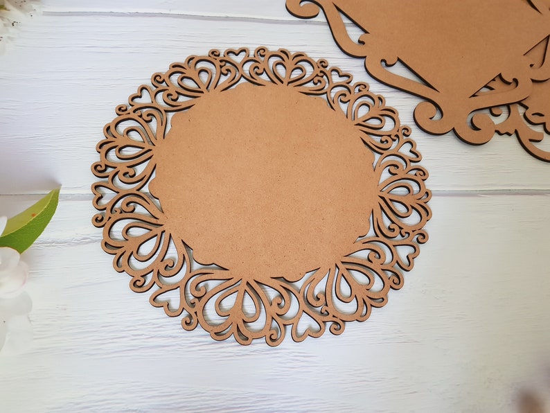 May include: A brown wooden round charger plate with a decorative, intricate, laser-cut design of hearts and swirls around the edge.