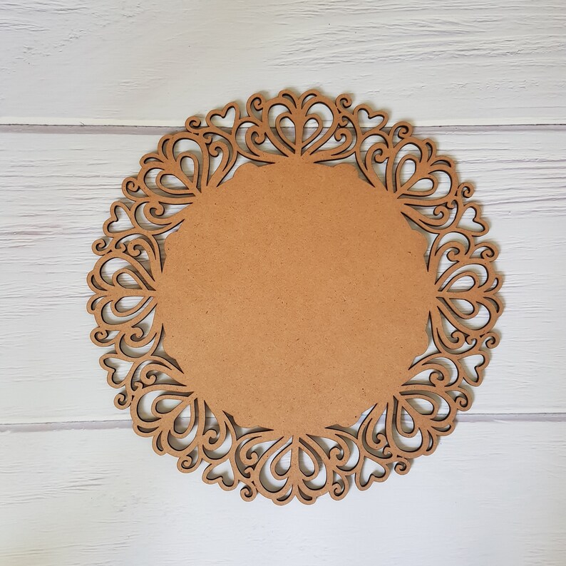 May include: A brown wooden round charger plate with a decorative lace design. The plate has a smooth, unfinished surface.