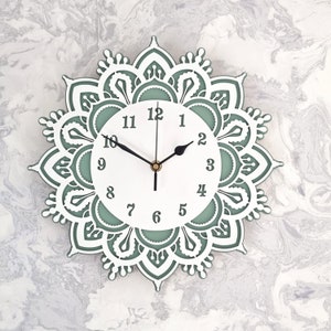 May include: A white clock face with black hands and black numbers set within a green mandala design. The clock face has a green background.