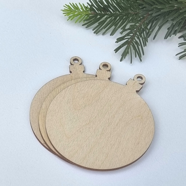 May include: Three unfinished wooden ornaments shaped like Christmas tree baubles. The ornaments are stacked on top of each other.