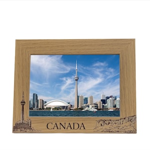 May include: A wooden picture frame with a photo of the Toronto skyline, including the CN Tower. The frame has a brown wood finish and the word "CANADA" is engraved below the photo.