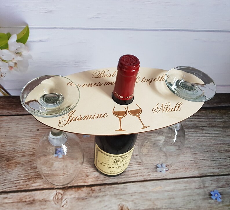 May include: Wooden wine bottle holder with two glass holders. The holder has the text "Best ones we've got together" and the names "Jasmine" and "Niall" engraved on it.